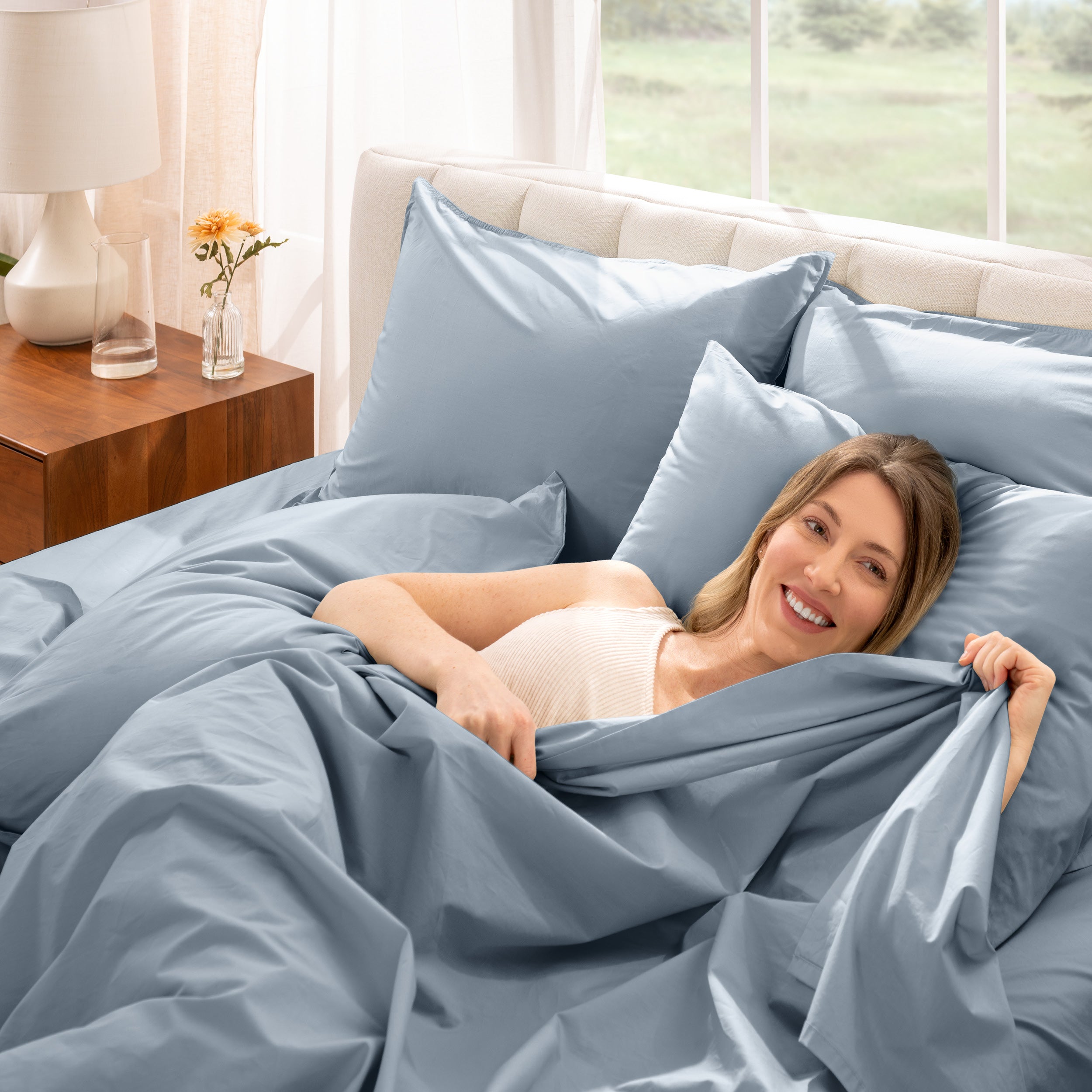 Woman lying in bed under percale sheets with a bright room setting