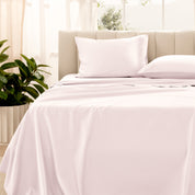 Organic sateen bedding on a bed with a beige headboard and plant in the corner.