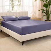 Organic cotton fitted sheet on a bed in a bedroom with a plant and window in the background