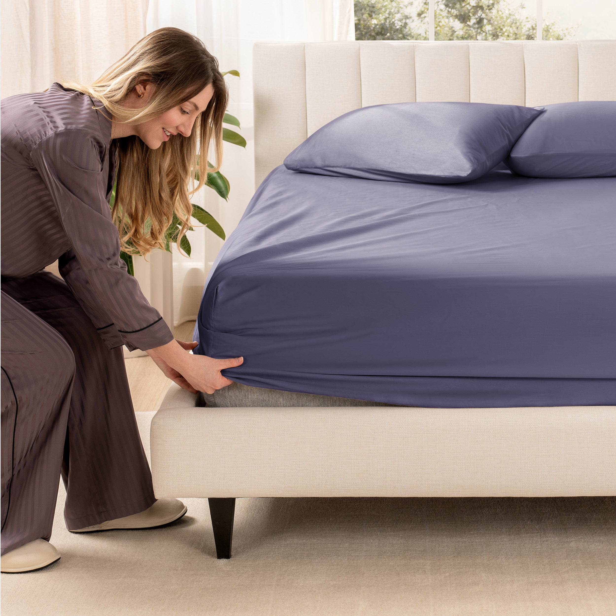 A woman is putting a fitted sheet on a mattress