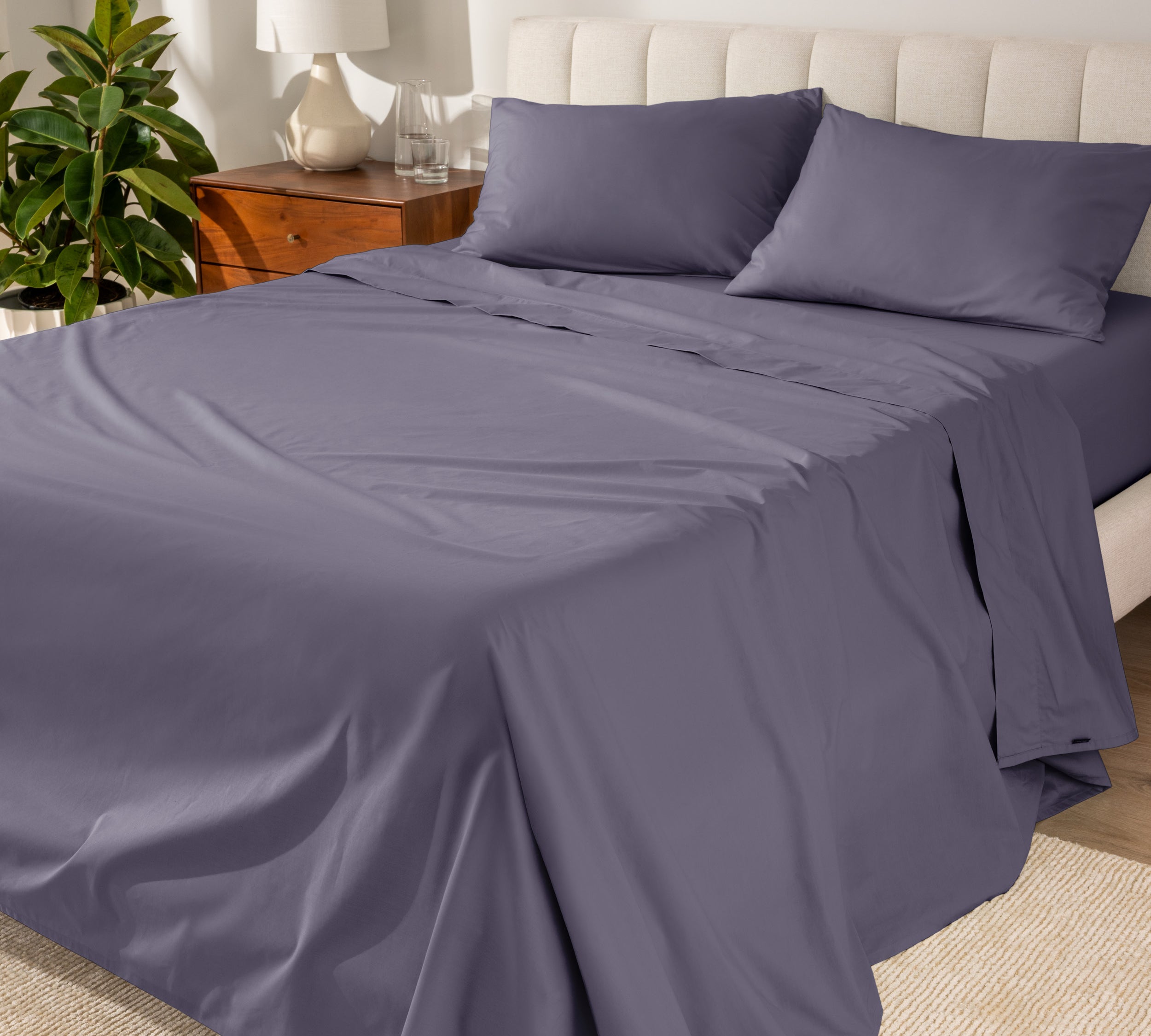 Organic cotton percale sheet set on a bed, with a flat sheet, fitted sheet, and two pillowcases displayed.