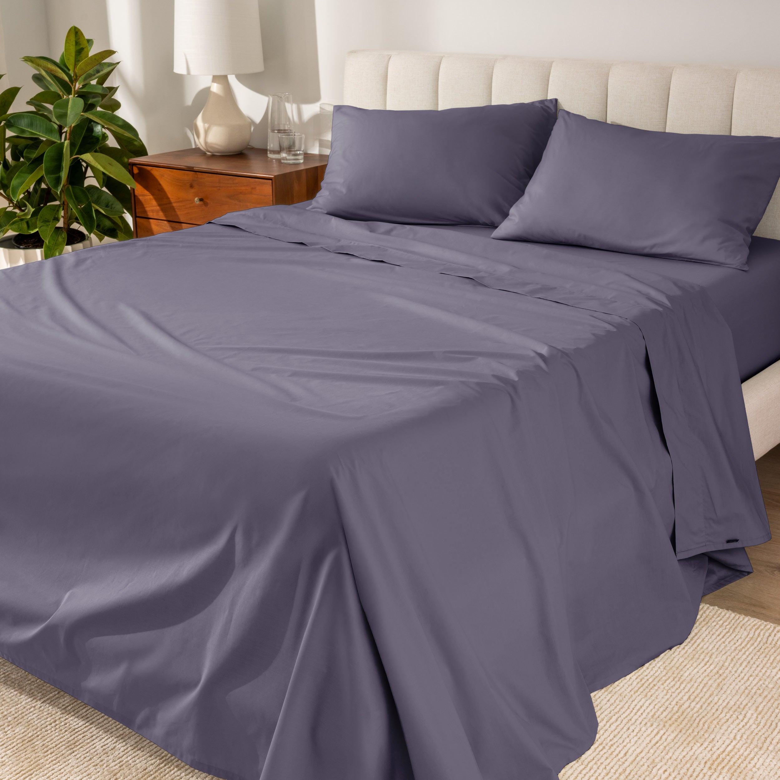 Organic cotton percale sheet set on a bed, with a flat sheet, fitted sheet, and two pillowcases displayed.