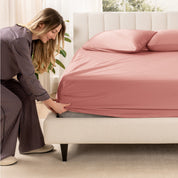 A woman is putting a fitted sheet on a mattress