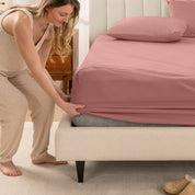 A women is putting on the percale fitted sheet on the bed