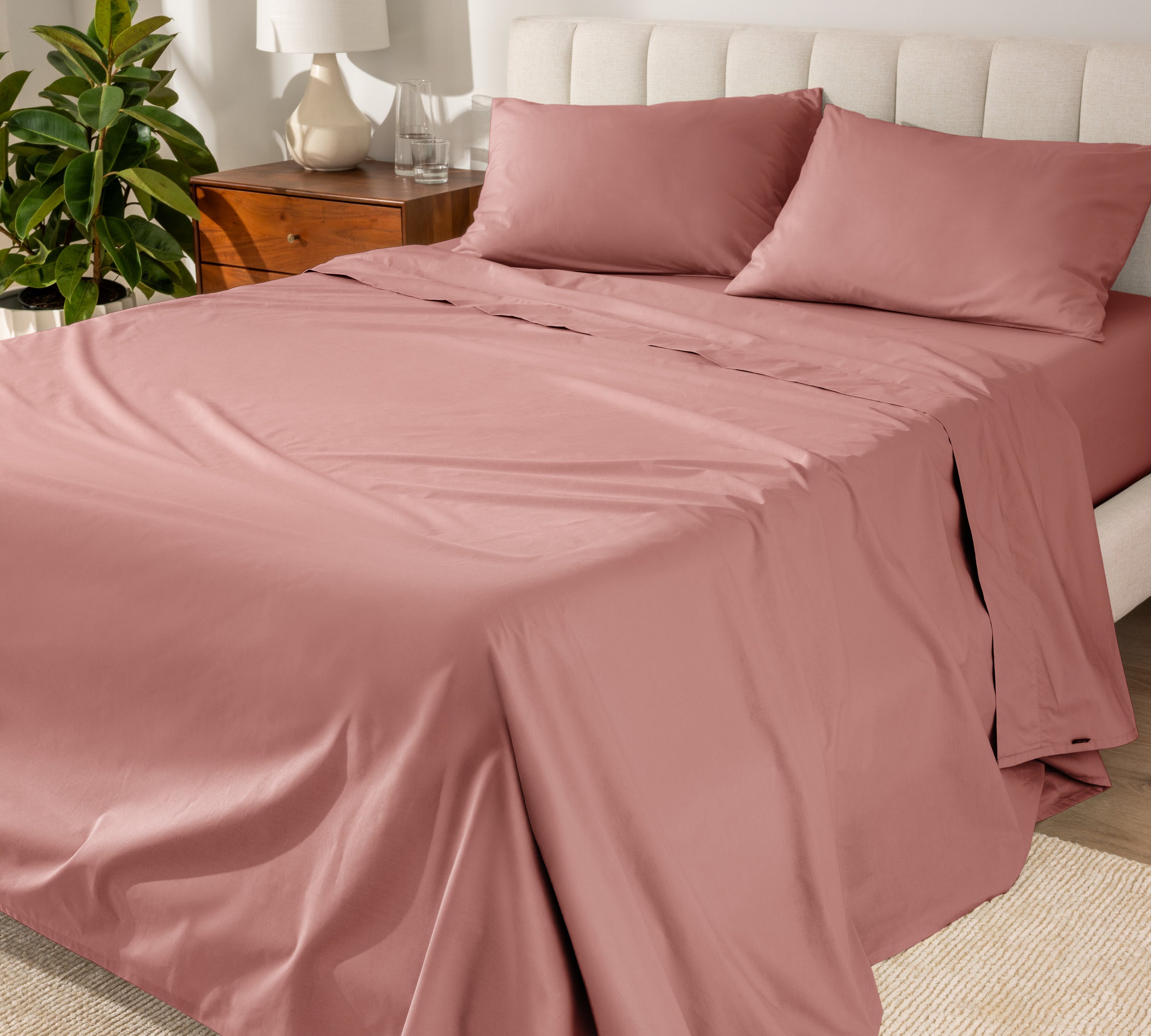 Organic cotton percale sheet set on a bed, with a flat sheet, fitted sheet, and two pillowcases displayed.