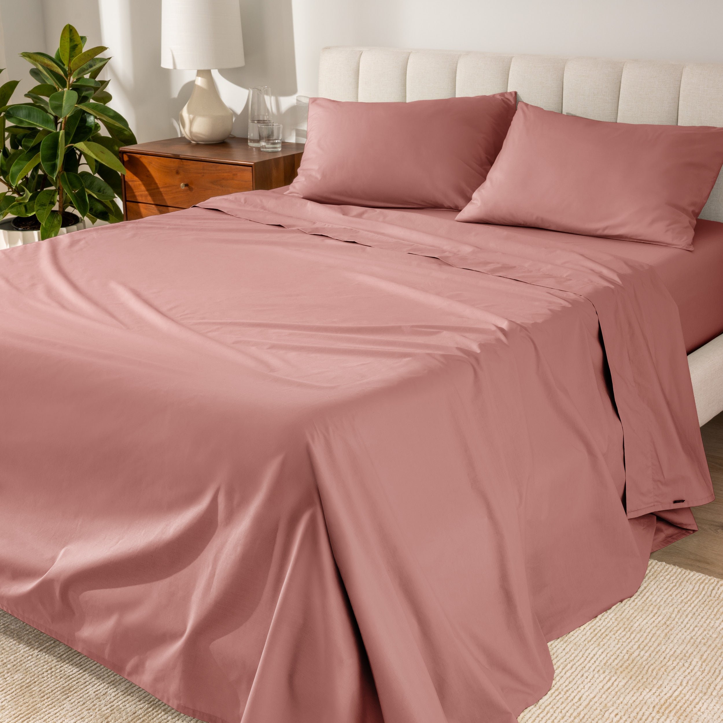 Organic cotton percale sheet set on a bed, with a flat sheet, fitted sheet, and two pillowcases displayed.