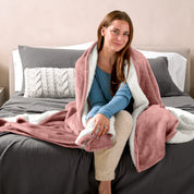 Woman cuddling with a sherpa blanket while sitting on the end of a bed