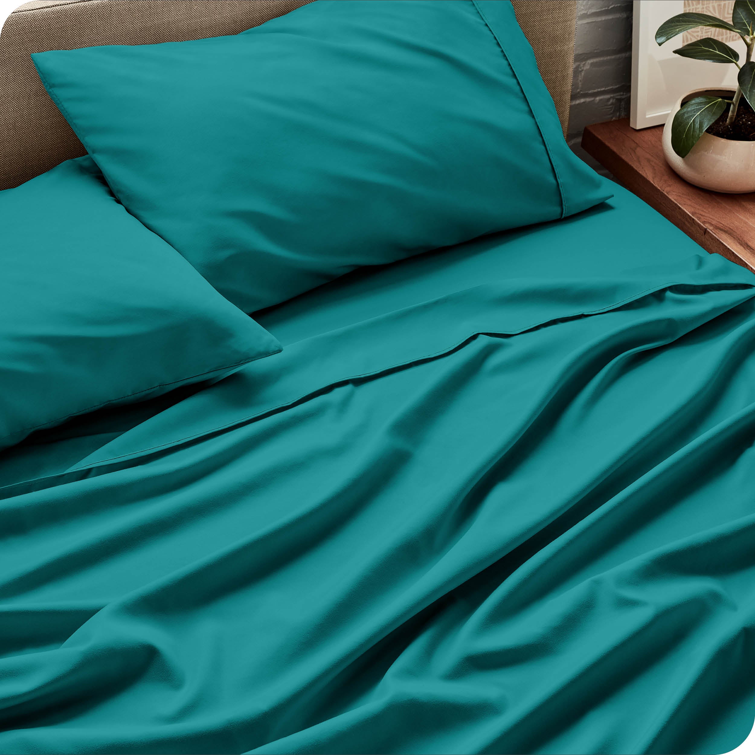 Microfiber sheets and matching pillowcases on a bed next to a large plant