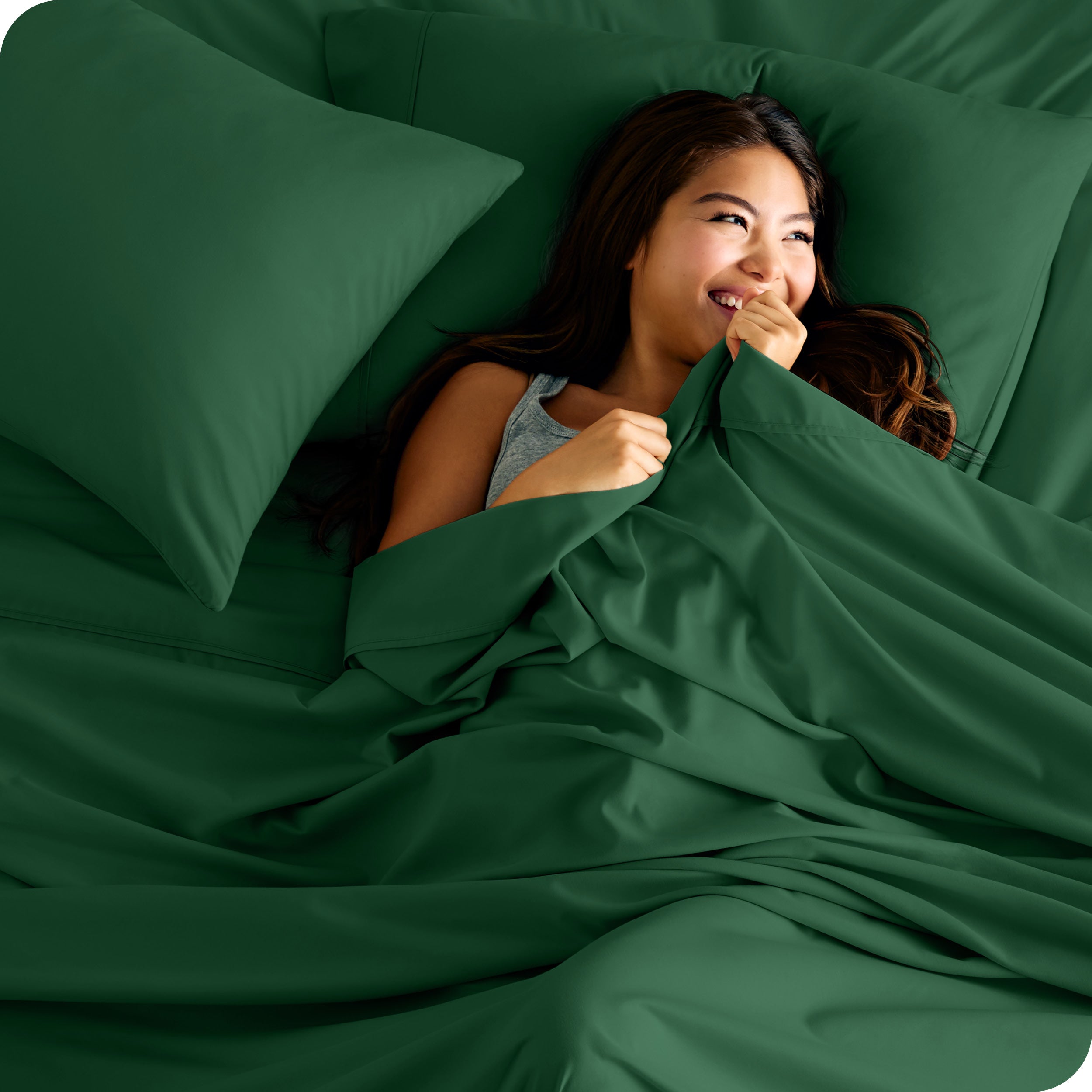 A smiling woman on a bed with a microfiber sheet over her