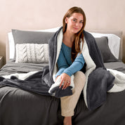 Woman cuddling with a sherpa blanket while sitting on the end of a bed
