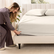 A woman is putting a fitted sheet on a mattress