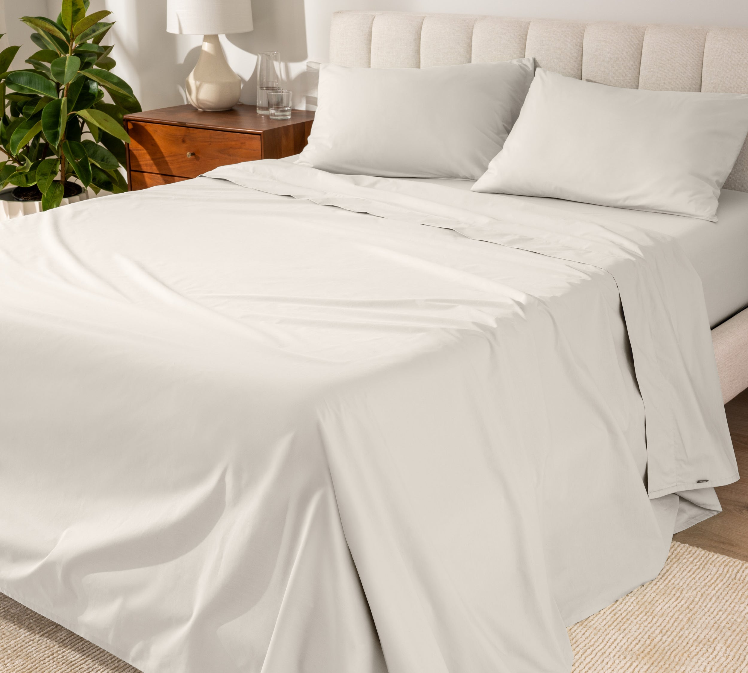 Organic cotton percale sheet set on a bed, with a flat sheet, fitted sheet, and two pillowcases displayed.