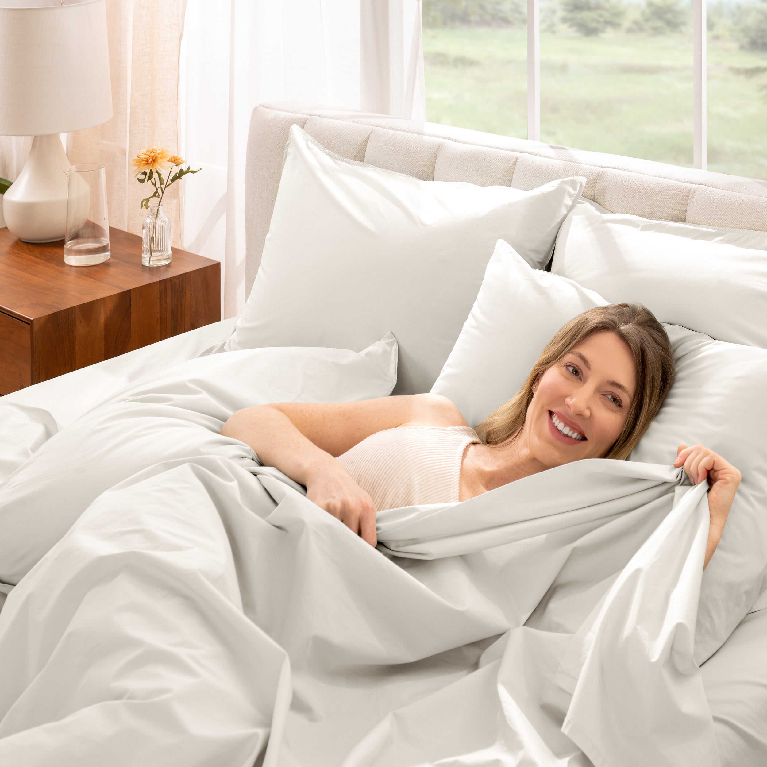 Woman lying in bed under percale sheets with a bright room setting