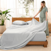 Woman arranging linen sheets on a wooden bed in a bright room with plants.