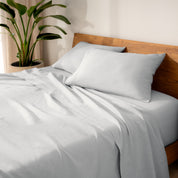 Linen bed sheets and pillows on a wooden bed with a plant in the background