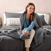 Woman cuddling with a sherpa blanket while sitting on the end of a bed