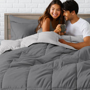 A couple sitting in a bed made with a reversible comforter and sheet set