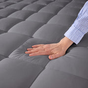 A hand is feeling the soft cotton texture of the mattress pad.