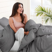 A woman sitting on a bed, wrapped in a comforter featuring the Bare Home flannel duvet set.