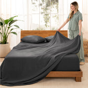 Woman arranging linen sheets on a wooden bed in a bright room with plants.