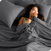 A smiling woman on a bed with a microfiber sheet over her