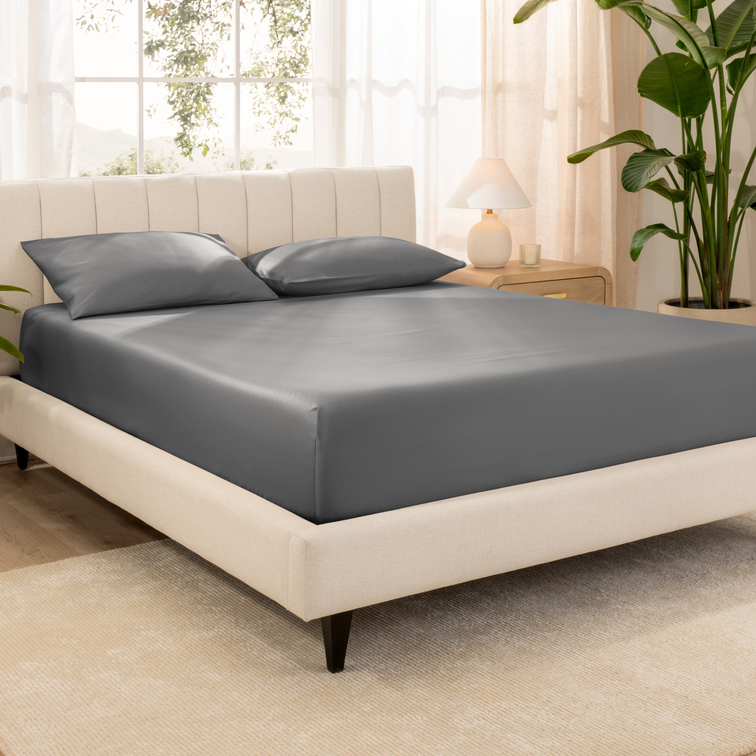 Organic cotton fitted sheet on a bed in a bedroom with a plant and window in the background