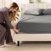 A woman is putting a fitted sheet on a mattress