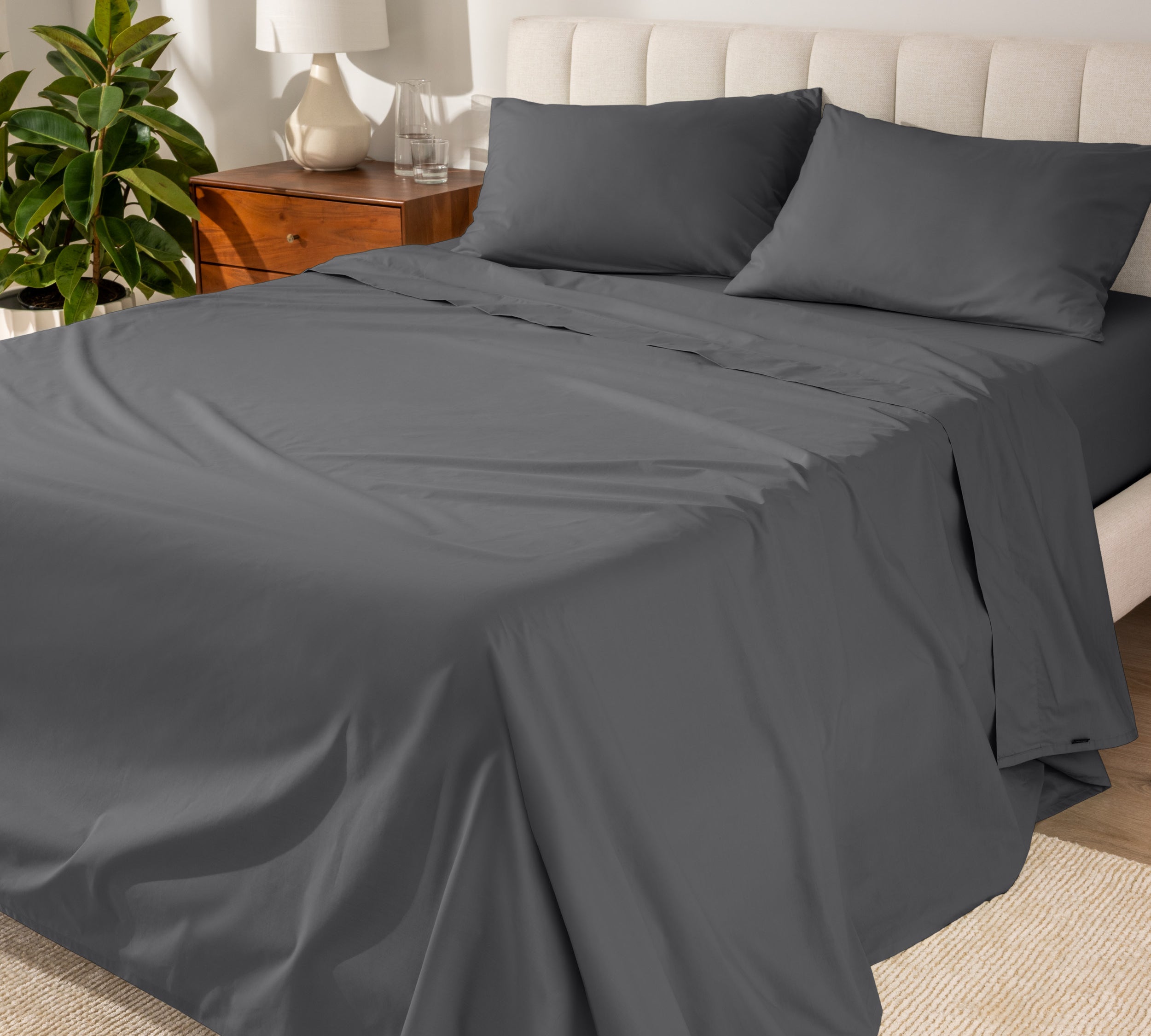 Organic cotton percale sheet set on a bed, with a flat sheet, fitted sheet, and two pillowcases displayed.