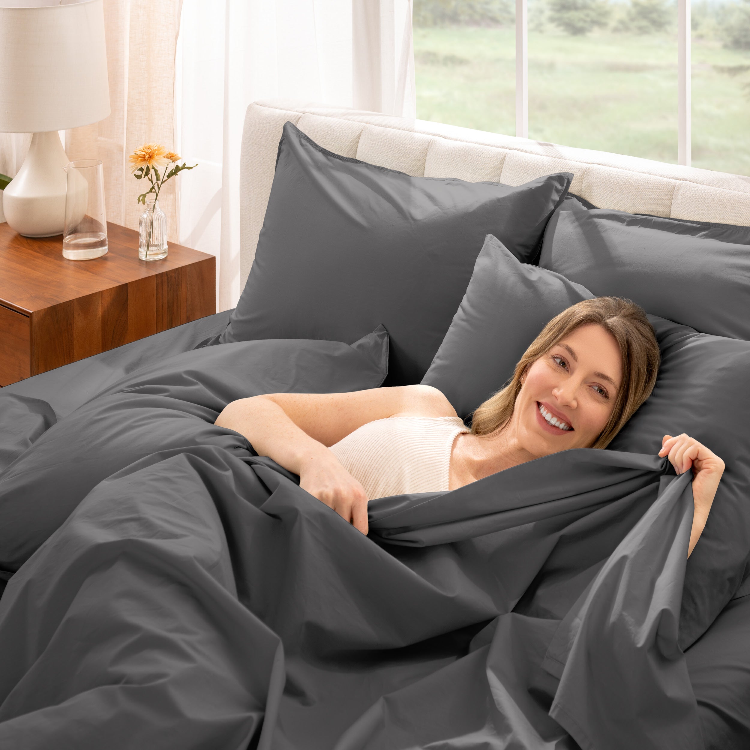 Woman lying in bed under percale sheets with a bright room setting