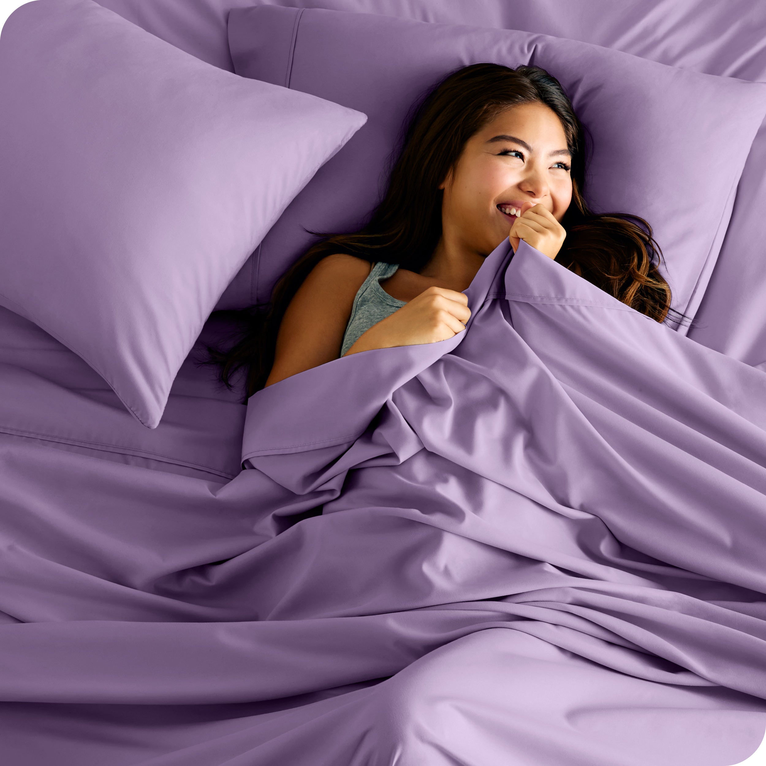A smiling woman on a bed with a microfiber sheet over her