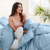 A woman sitting on a bed, wrapped in a comforter featuring the Bare Home flannel duvet set.
