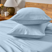 Two pillows with flannel pillowcases stacked on a bed with a wooden headboard and side table in the background.