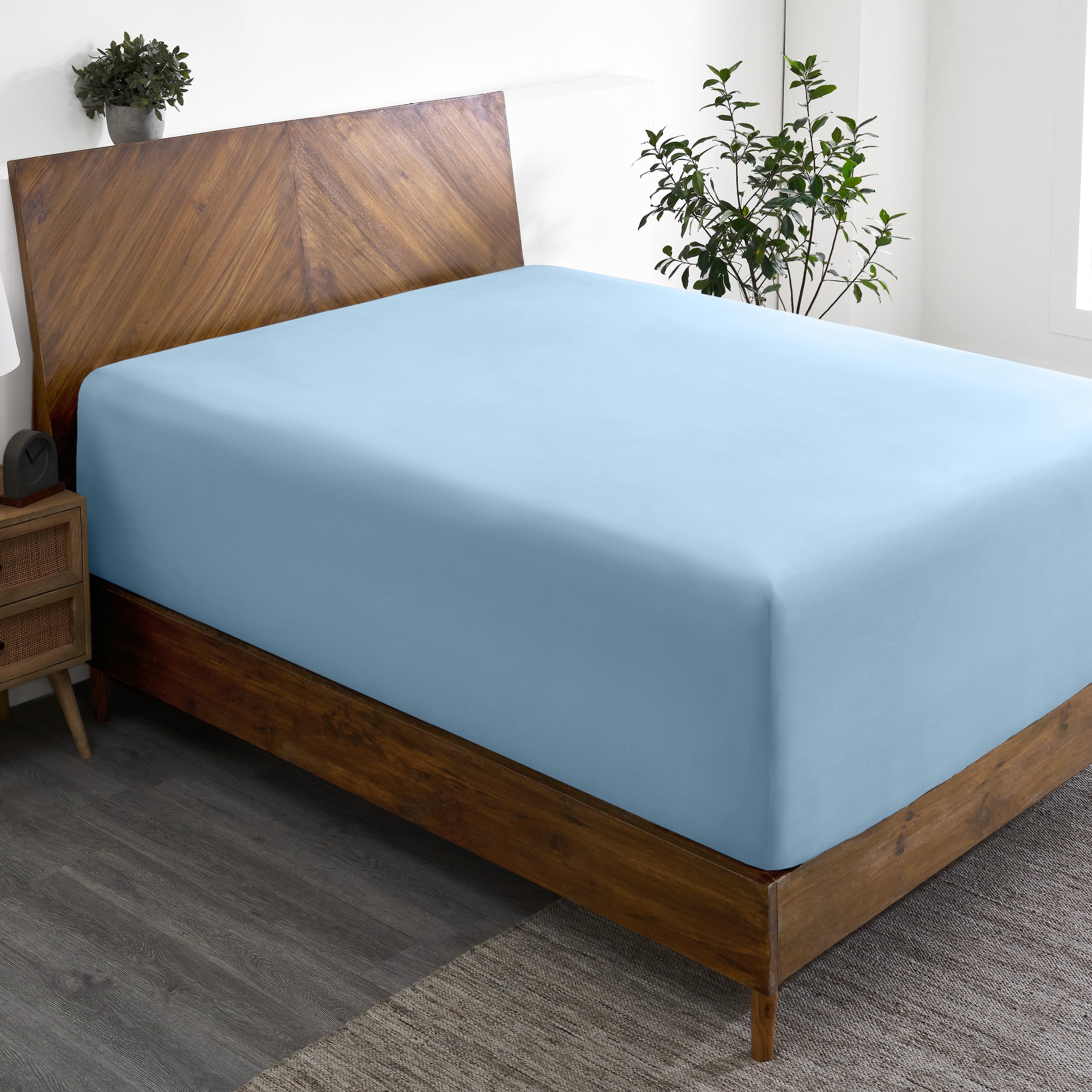 A wide corner view of a modern bed made with a microfiber fitted sheet on the mattress.