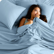 A smiling woman on a bed with a microfiber sheet over her