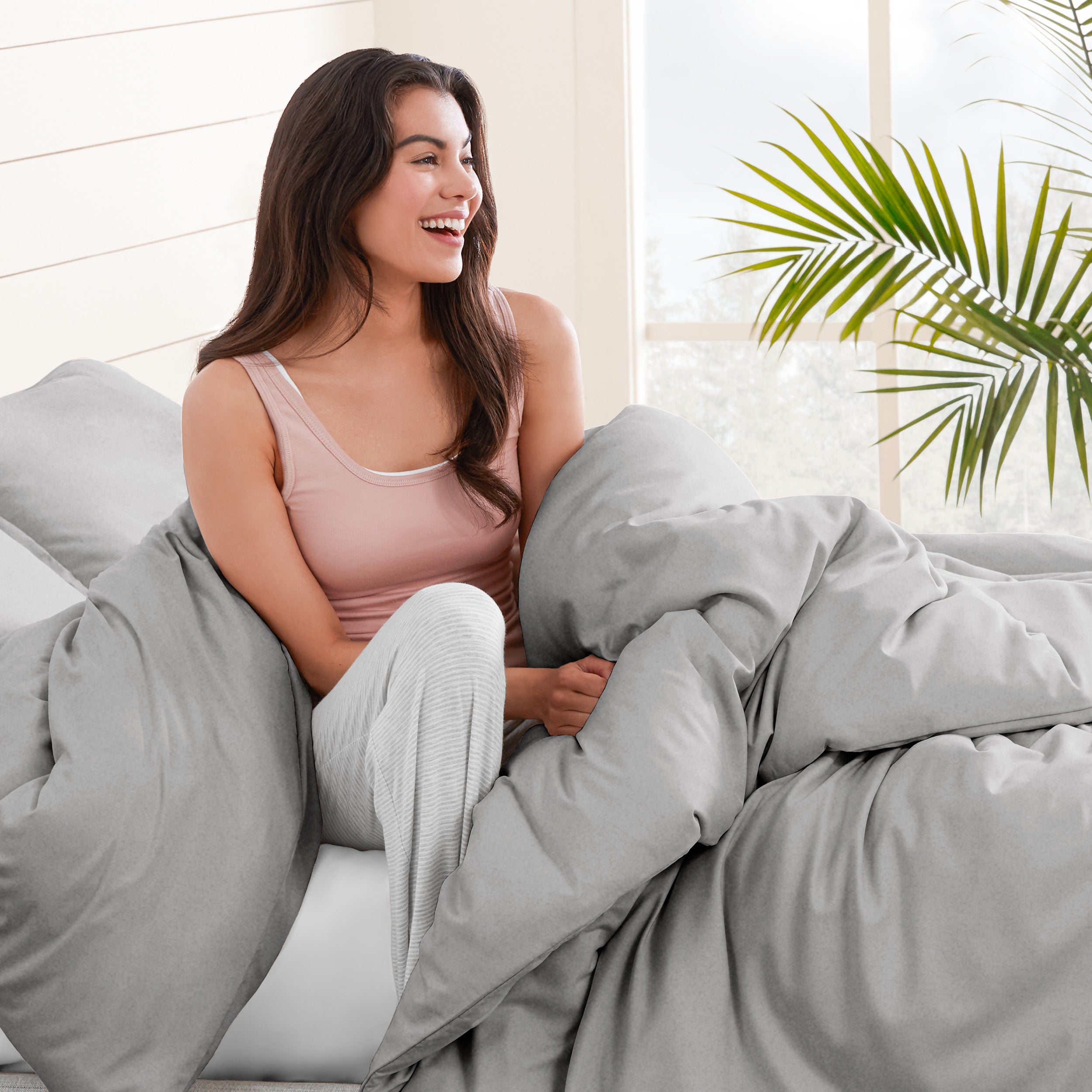 A woman sitting on a bed, wrapped in a comforter featuring the Bare Home flannel duvet set.