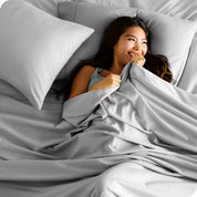 A smiling woman on a bed with a microfiber sheet over her