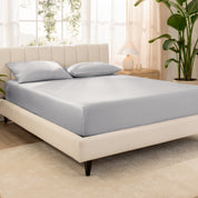 Organic cotton fitted sheet on a bed in a bedroom with a plant and window in the background
