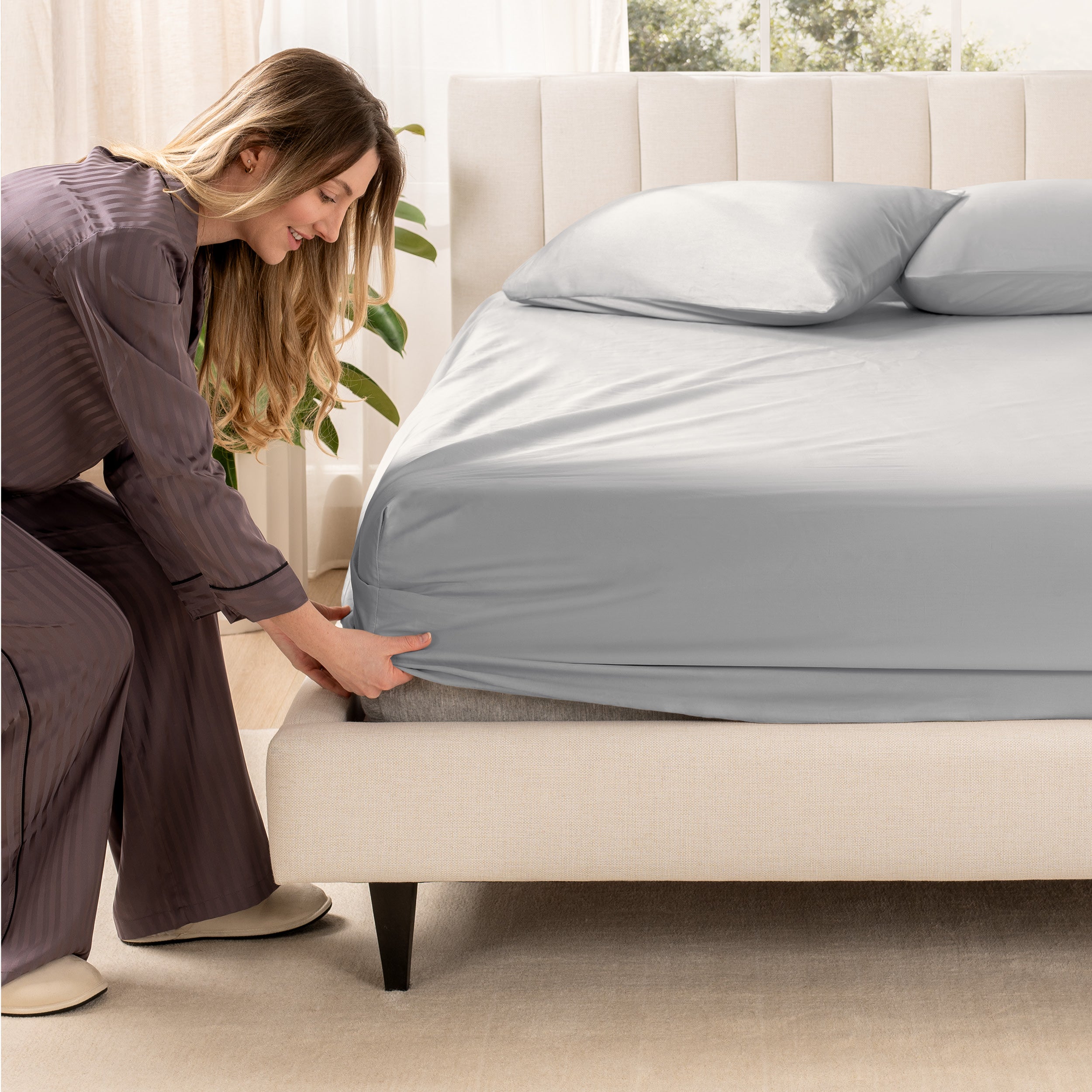 A woman is putting a fitted sheet on a mattress