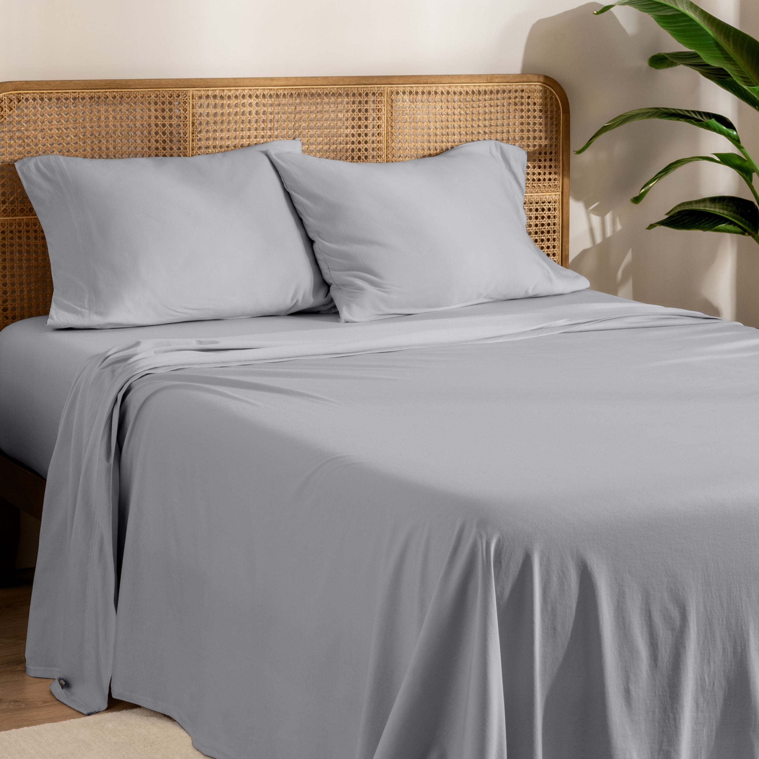 Organic jersey sheets and pillowcases on a bed with plants on the side in a bright and chill room scene.