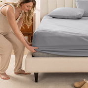 A women is putting on the percale fitted sheet on the bed