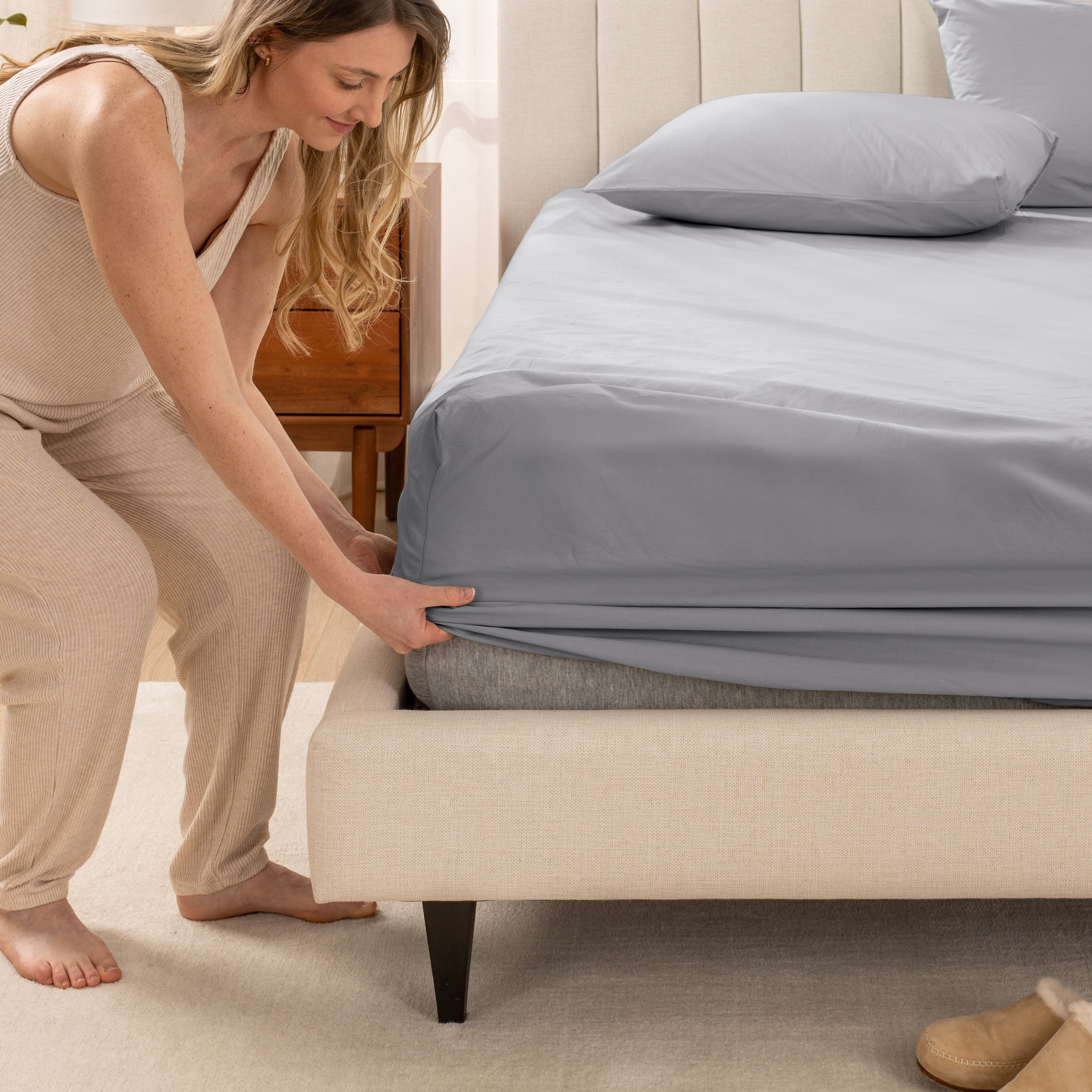 A women is putting on the percale fitted sheet on the bed