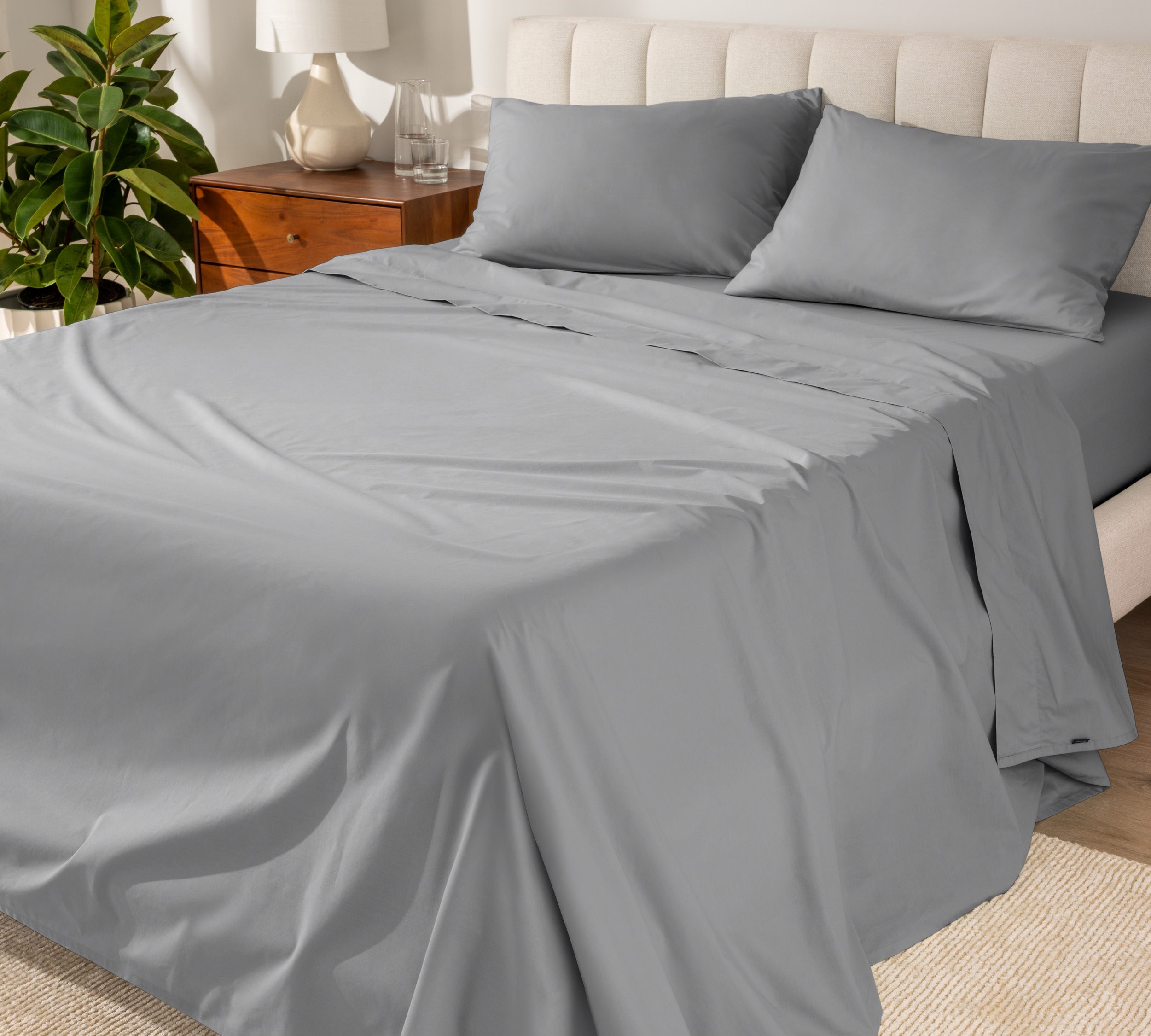 Organic cotton percale sheet set on a bed, with a flat sheet, fitted sheet, and two pillowcases displayed.