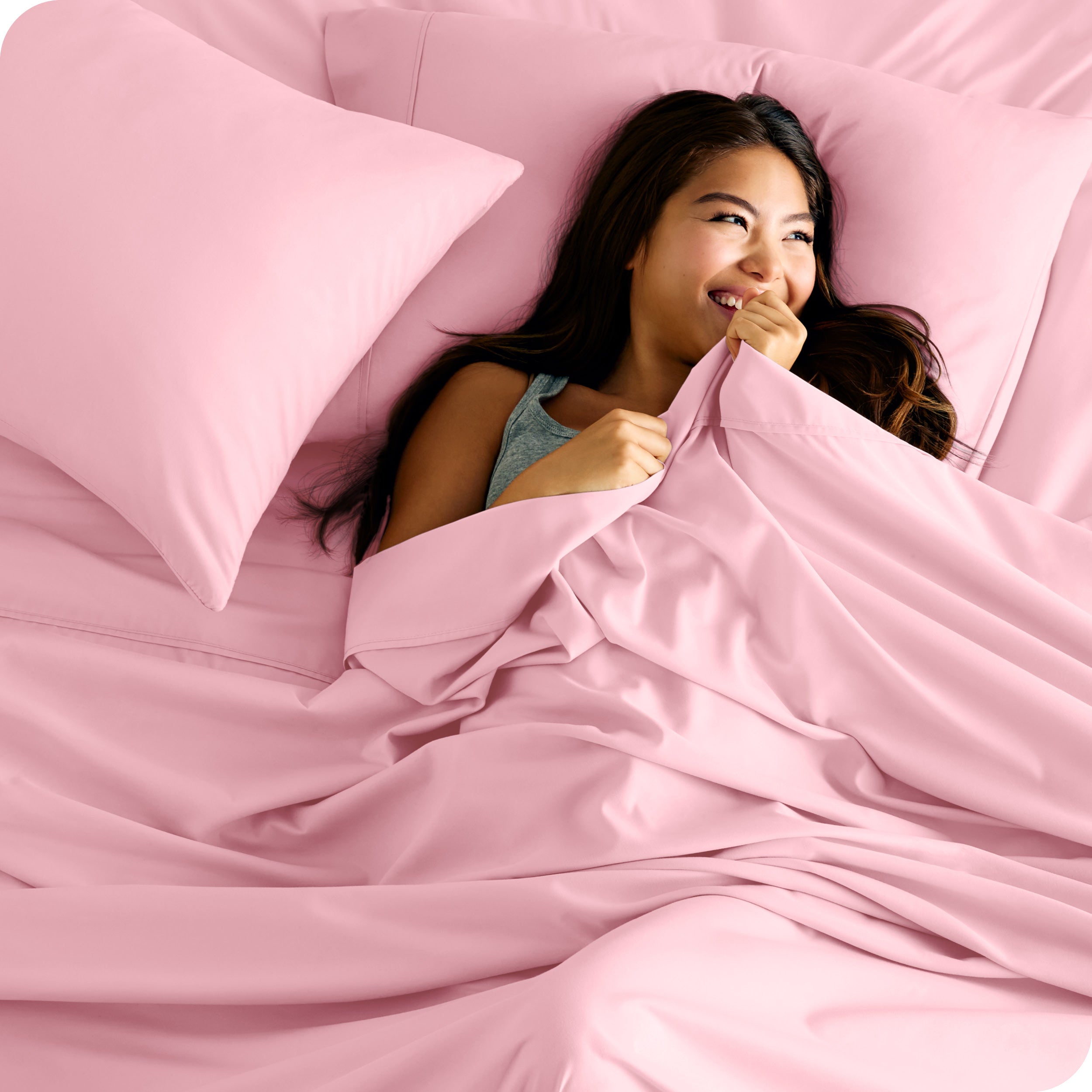 A smiling woman on a bed with a microfiber sheet over her