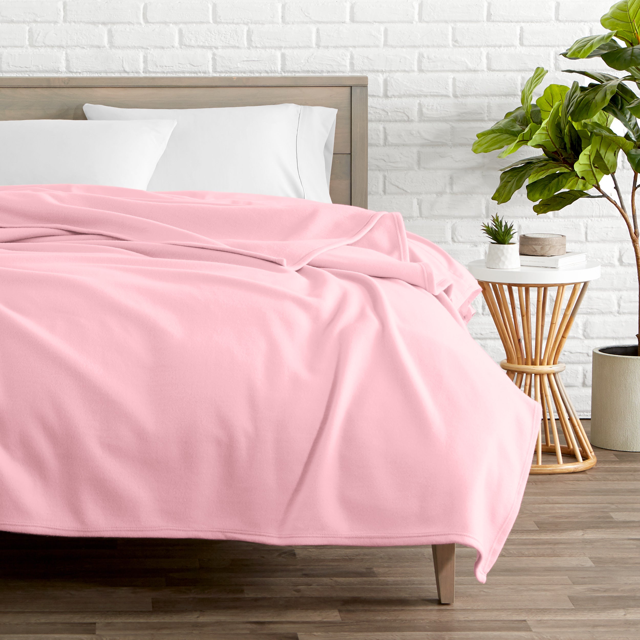 A polar fleece blanket on a bed next to a table and a large plant