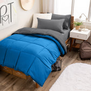 A wooden bed frame with a reversible comforter and sheet set on the mattress in a dorm style room.
