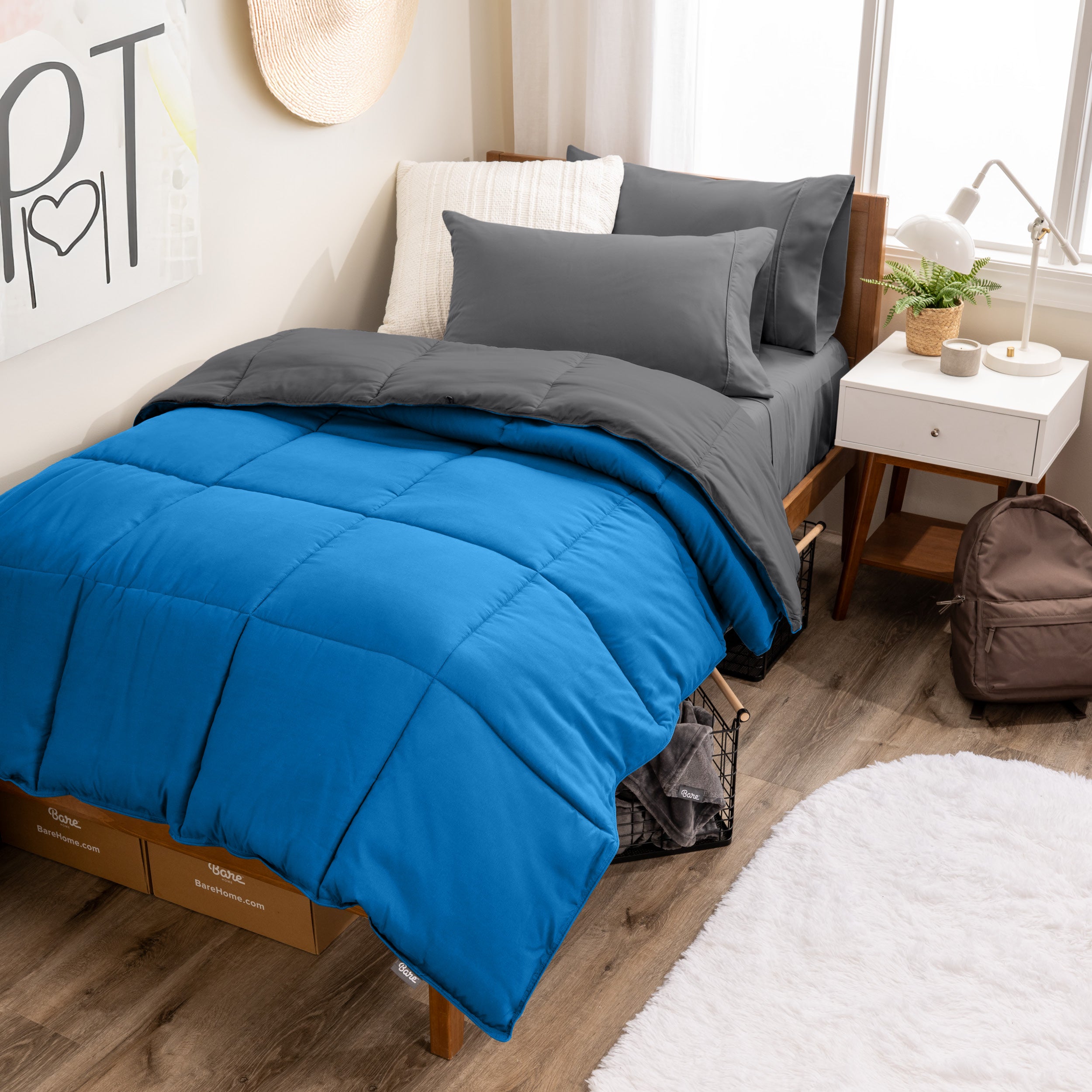 A wooden bed frame with a reversible comforter and sheet set on the mattress in a dorm style room.
