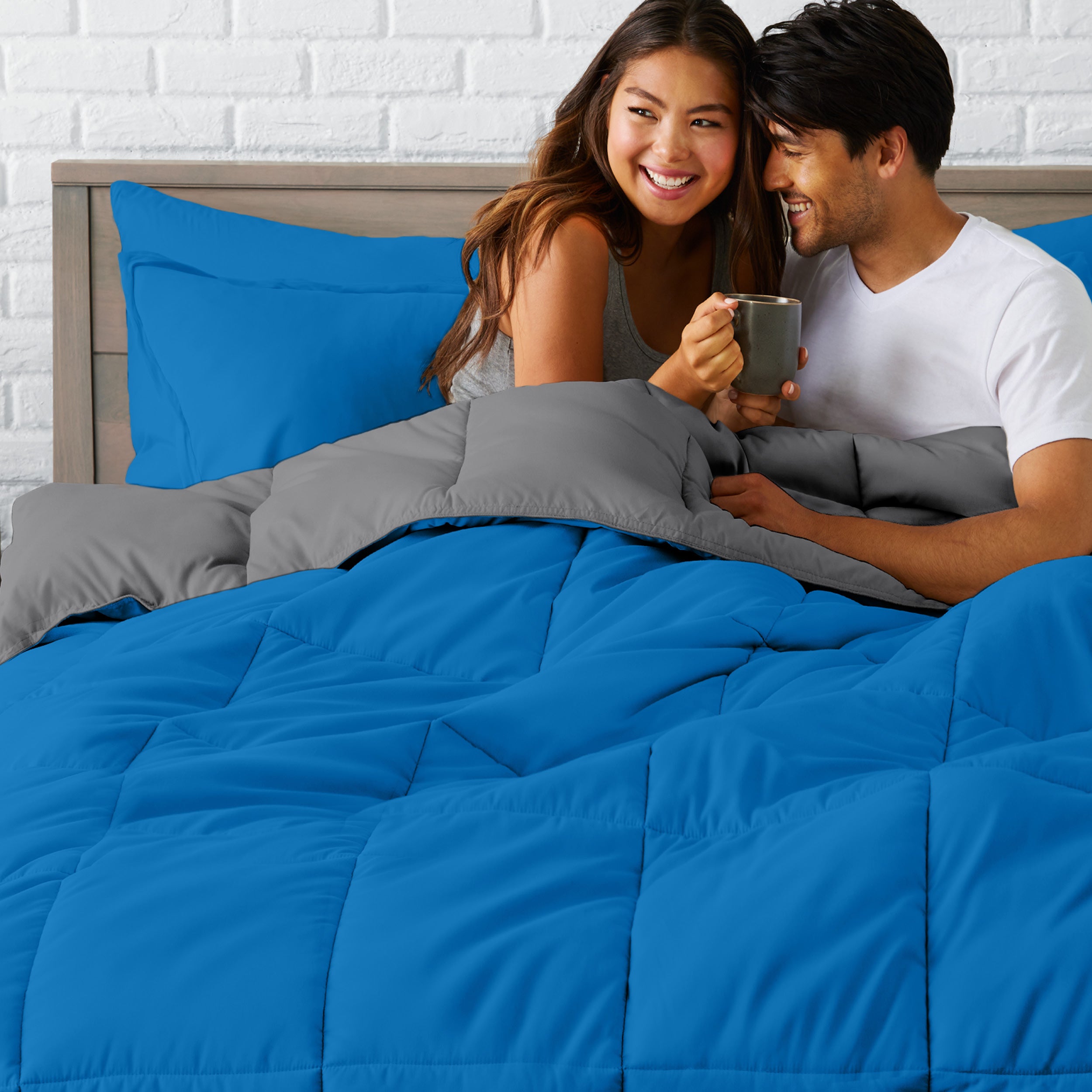 A couple sitting in a bed made with a reversible comforter and sheet set