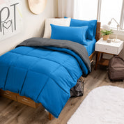 A wooden bed frame with a reversible comforter and sheet set on the mattress in a dorm style room.