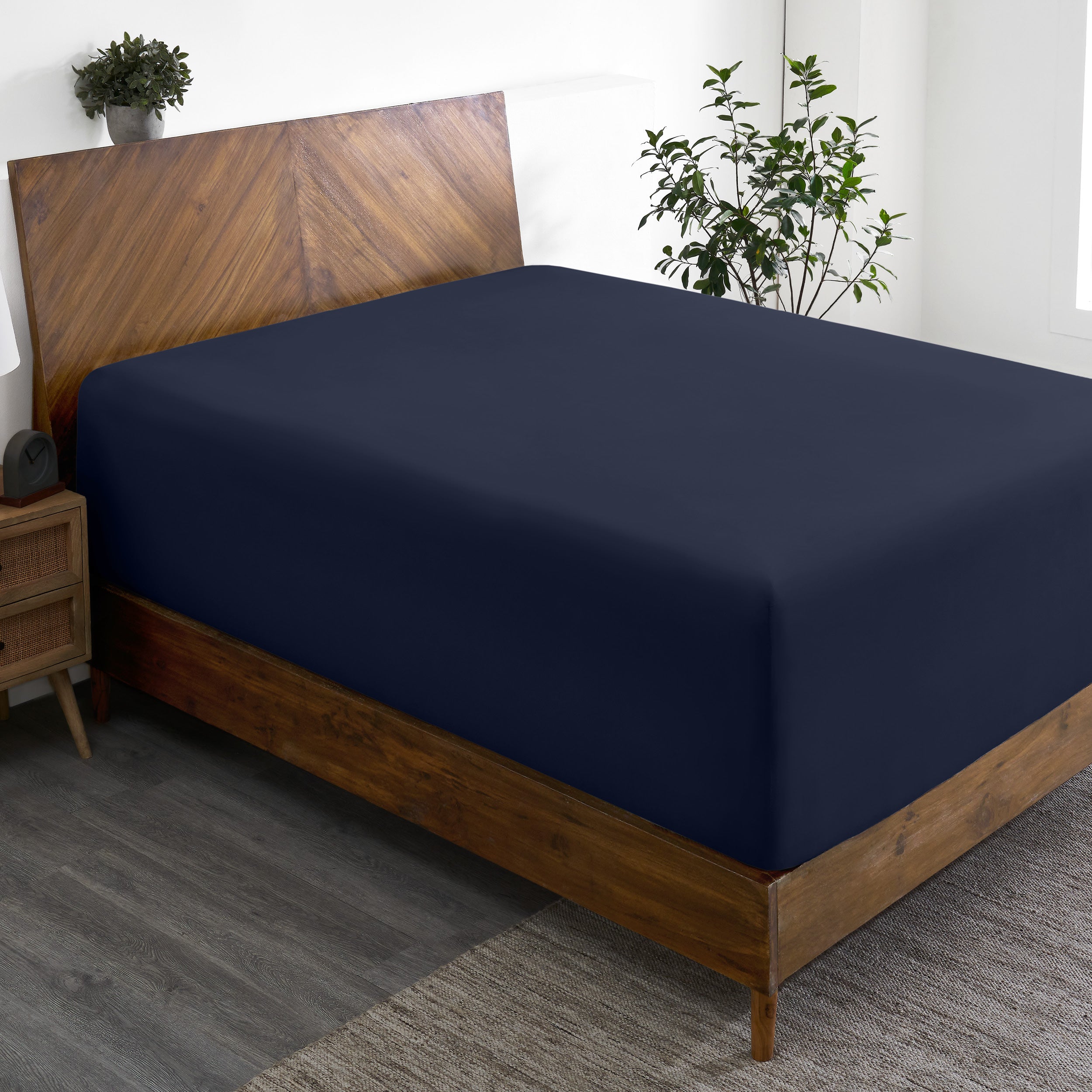 A wide corner view of a modern bed made with a microfiber fitted sheet on the mattress.