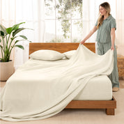 Woman arranging linen sheets on a wooden bed in a bright room with plants.
